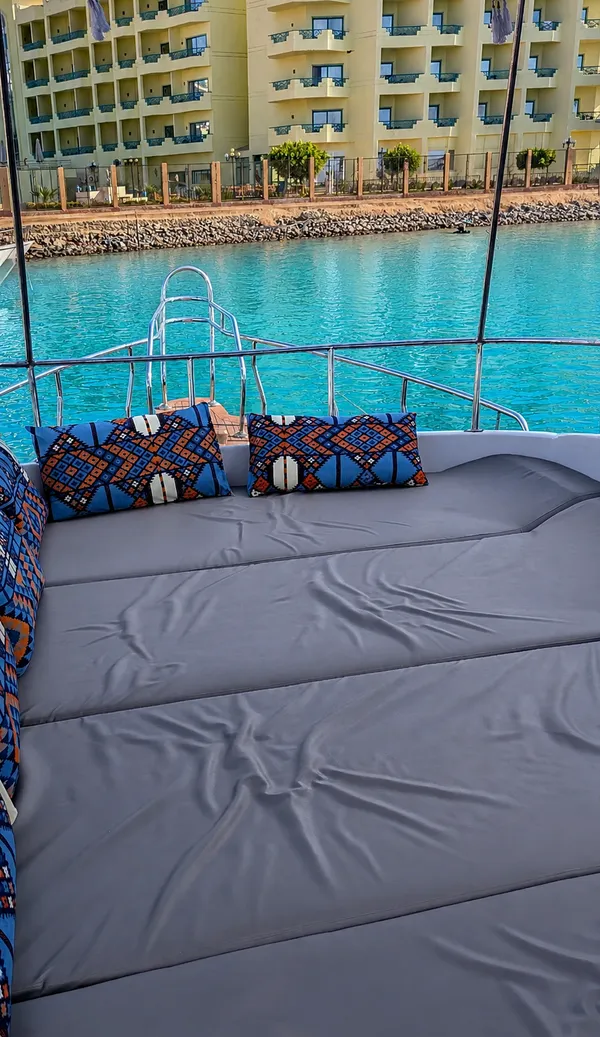 Sonnendeck mit gepolsterter Liegefläche und gemusterten Kissen, dahinter das Wasser der Marina